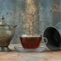 Stary, zdobiony czajniczek i szklanka z herbatą na tle rustykalnej ściany.
