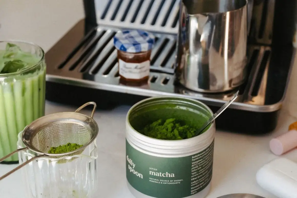 Puszka z zielonym proszkiem matcha, sitko z proszkiem, szklanka z napojem i ekspres do kawy.